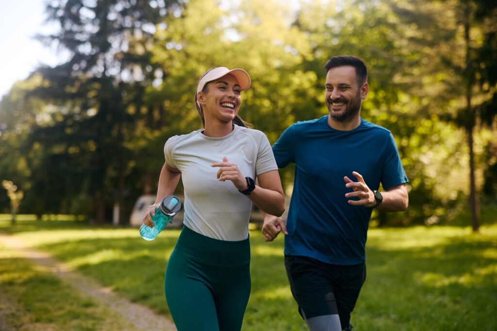 Fröhliches sportliches Paar joggt durch den Park