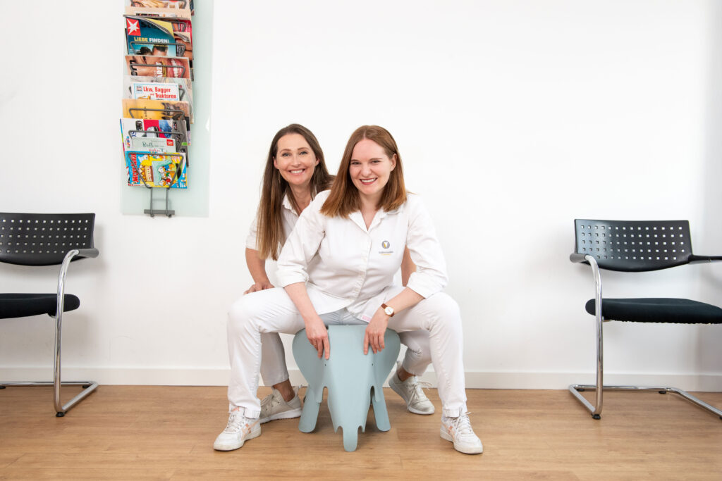 Dr. Nadja Bottenberg und Dr. Anne Sturmes auf dem Elefanten-Hocker im Wartezimmer der Praxis in Taunusstein