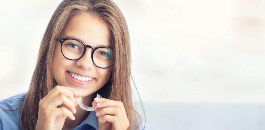 Junges Mädchen mit Brille hält eine unsichtbare Zahnspange