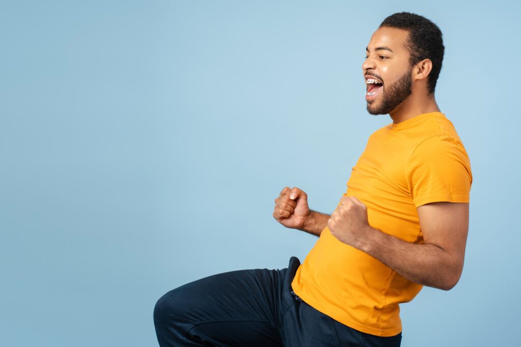Junger Mann im orangefarbenen T-Shirt jubelt vor blauem Hintergrund